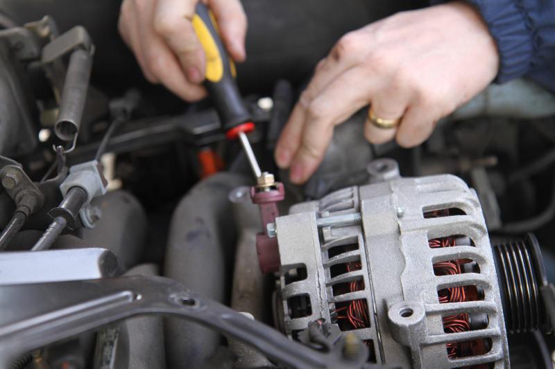 Man removing a faulty car alternator with a screwdriver to fix it.