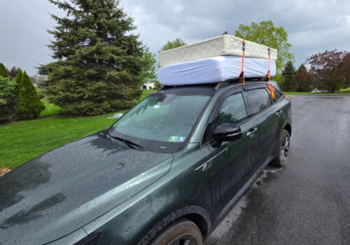 A car driving with two mattresses tied to the roof rack.