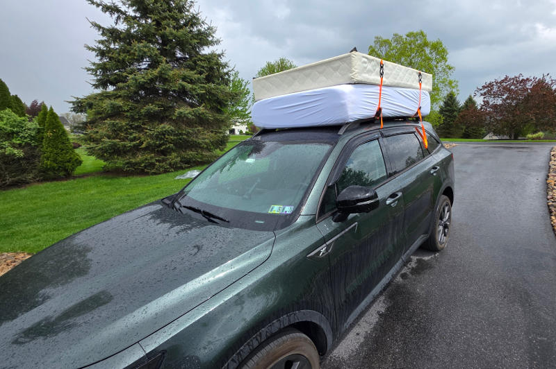 A car driving with two mattresses tied to the roof rack.